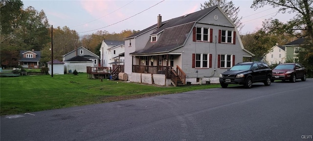 view of front of house with a gambrel roof, a porch, a chimney, and a front lawn