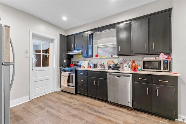 kitchen featuring under cabinet range hood, light countertops, decorative backsplash, appliances with stainless steel finishes, and light wood-style floors