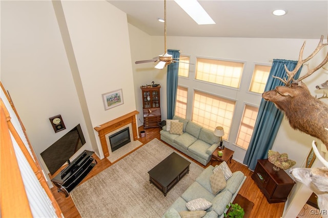 living room featuring a skylight, a fireplace with flush hearth, wood finished floors, and high vaulted ceiling