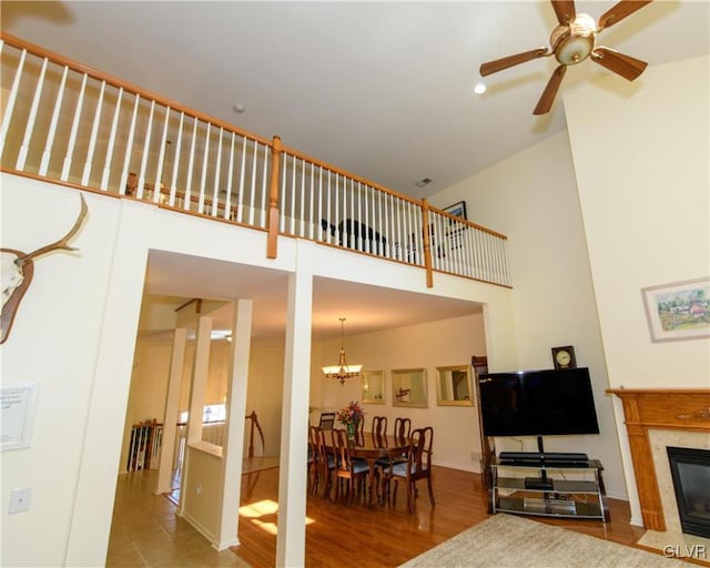 living area featuring a fireplace with flush hearth, a high ceiling, wood finished floors, and ceiling fan with notable chandelier