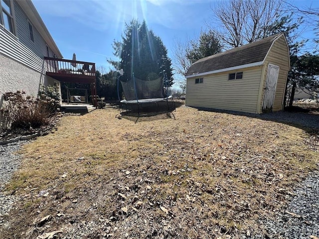 view of yard featuring a wooden deck, an outbuilding, a trampoline, and a shed