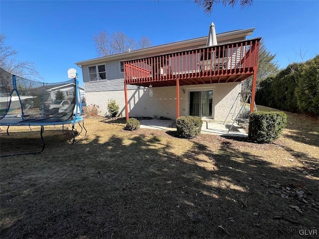 rear view of property featuring a deck, a trampoline, and stucco siding