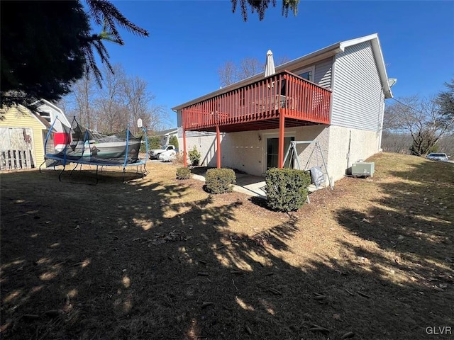 rear view of property with a trampoline, central air condition unit, stucco siding, a deck, and a patio area