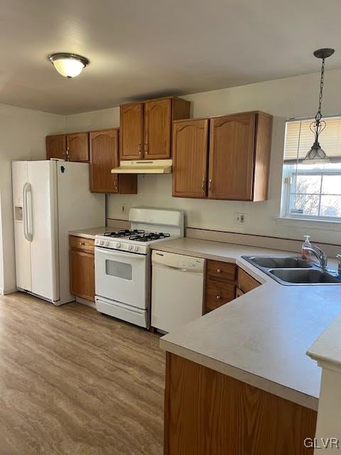 kitchen with white appliances, a sink, light countertops, under cabinet range hood, and decorative light fixtures