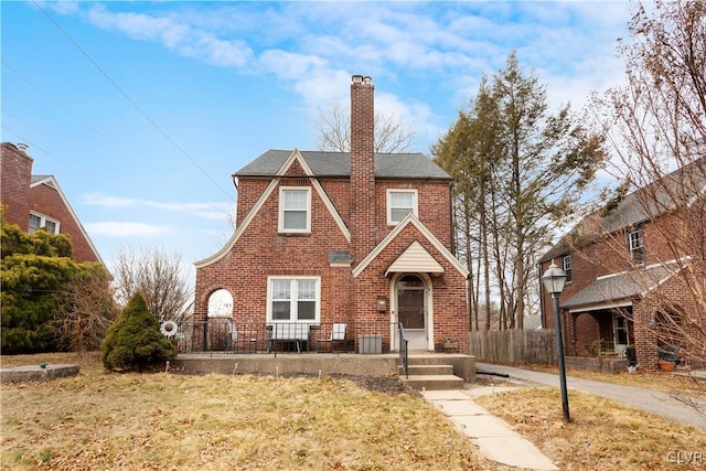 english style home with brick siding, cooling unit, a chimney, and roof with shingles