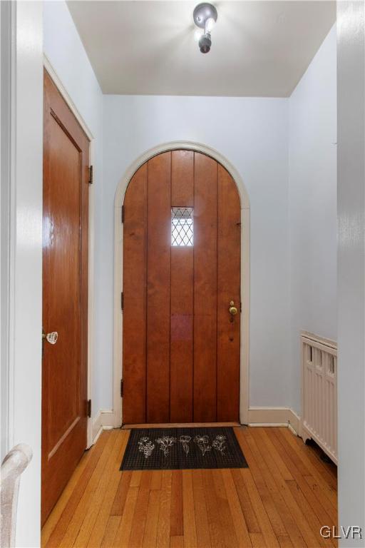 entrance foyer with arched walkways, baseboards, and light wood-style floors