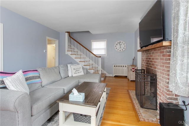 living area with radiator heating unit, stairway, a fireplace, light wood finished floors, and baseboards