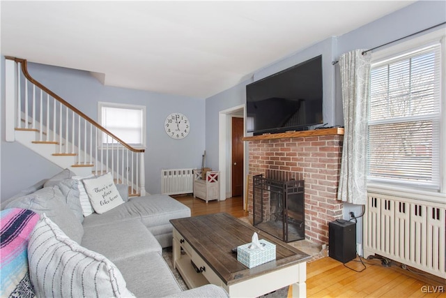 living area featuring stairway, a brick fireplace, radiator, and wood finished floors