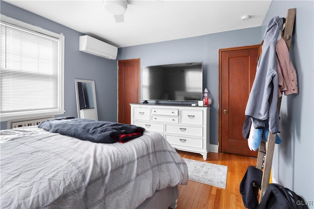 bedroom featuring ceiling fan, light wood-style floors, and a wall unit AC