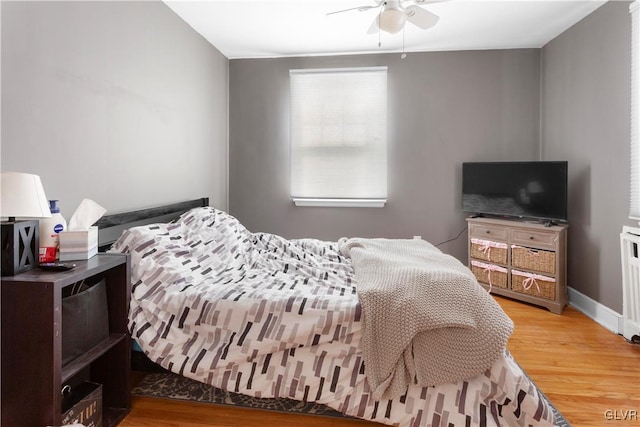 bedroom with ceiling fan, baseboards, radiator, and wood finished floors