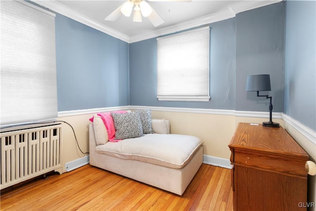 living area featuring wood finished floors, baseboards, radiator heating unit, ceiling fan, and crown molding