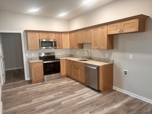 kitchen featuring light wood-type flooring, a sink, baseboards, appliances with stainless steel finishes, and light stone countertops