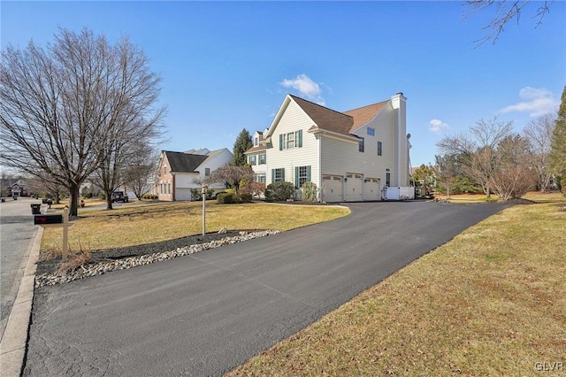 view of home's exterior with aphalt driveway, a yard, a chimney, and an attached garage