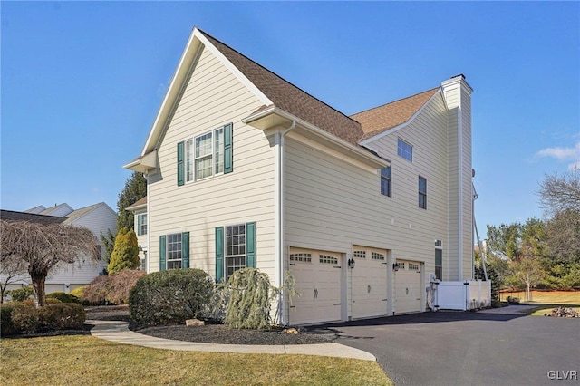 view of side of home featuring a garage, a chimney, driveway, and a shingled roof