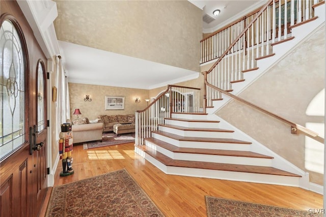 entryway with visible vents, crown molding, stairs, a high ceiling, and wood finished floors