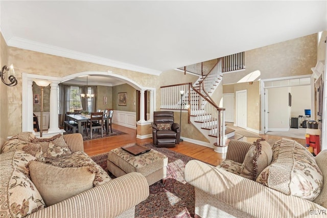 living area featuring ornamental molding, wood finished floors, stairway, arched walkways, and ornate columns