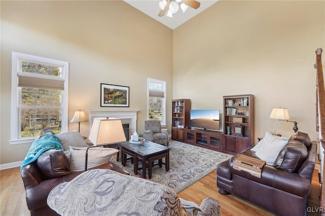 living area featuring a ceiling fan, wood finished floors, baseboards, high vaulted ceiling, and a premium fireplace