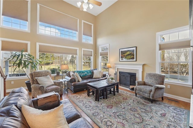 living room with wood finished floors, a towering ceiling, a fireplace, baseboards, and ceiling fan