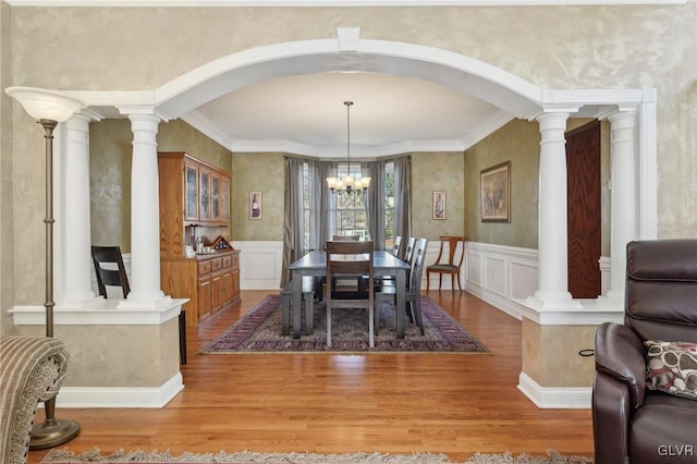 dining room with light wood-style flooring, a decorative wall, arched walkways, and ornate columns