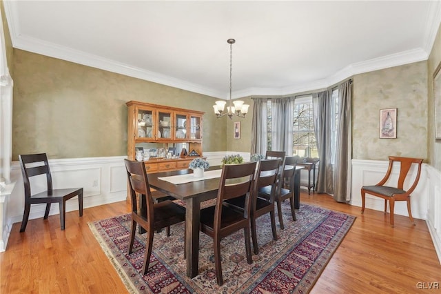 dining area with a notable chandelier, light wood-style floors, and a wainscoted wall