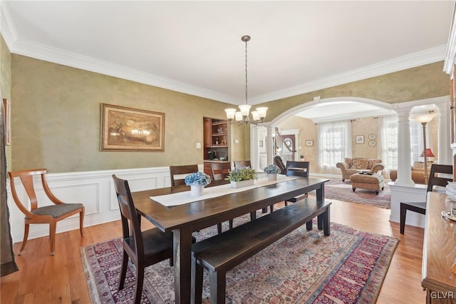 dining area with arched walkways, a wainscoted wall, light wood-type flooring, and ornate columns