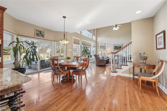 dining room featuring baseboards, stairs, light wood-style floors, a towering ceiling, and a ceiling fan