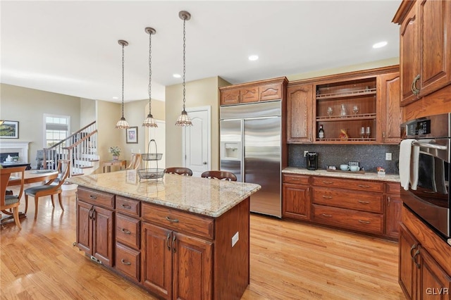 kitchen with a kitchen island, open shelves, a fireplace, light wood-style floors, and appliances with stainless steel finishes