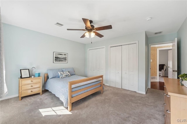 bedroom with a ceiling fan, visible vents, two closets, and carpet floors