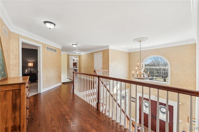 corridor with visible vents, a chandelier, ornamental molding, an upstairs landing, and wood finished floors