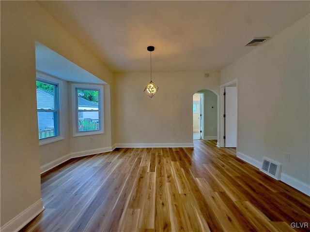 unfurnished dining area with arched walkways, visible vents, baseboards, and wood finished floors