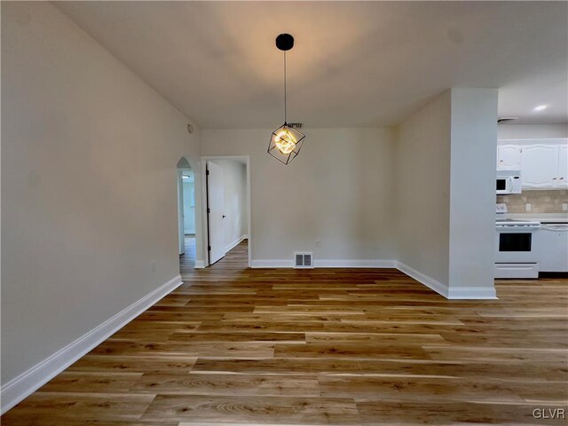 unfurnished dining area with arched walkways, visible vents, baseboards, and wood finished floors