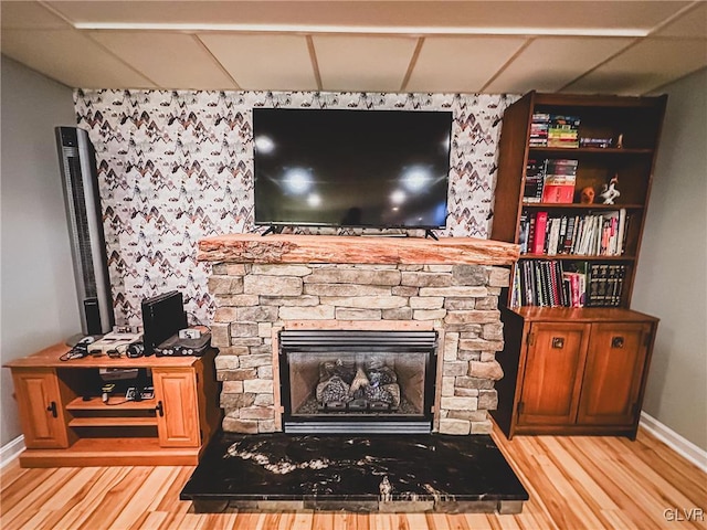 interior space with a stone fireplace, a paneled ceiling, baseboards, and wood finished floors