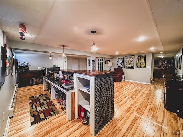 kitchen featuring dark countertops, baseboards, open floor plan, light wood-style floors, and hanging light fixtures