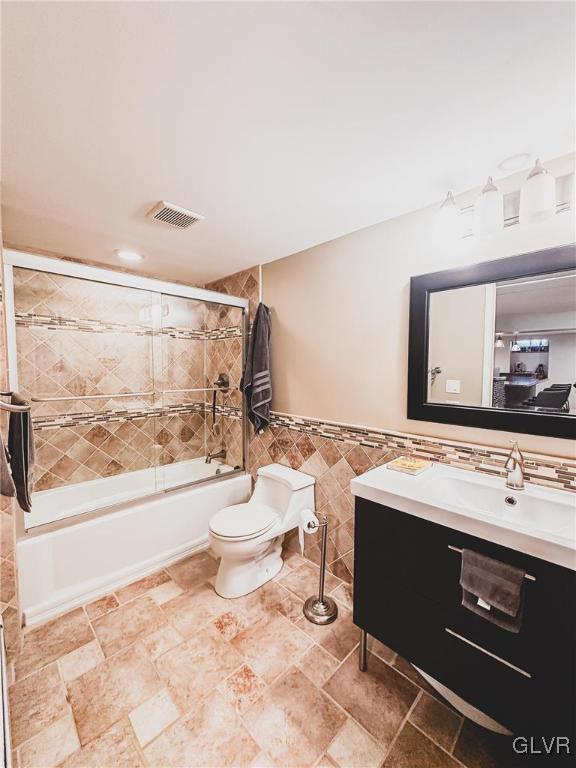 bathroom featuring vanity, visible vents, tile walls, toilet, and combined bath / shower with glass door