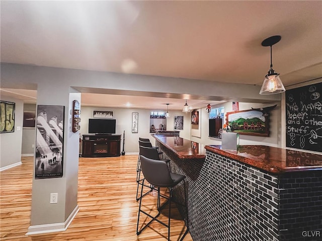 bar featuring a dry bar, decorative light fixtures, light wood-style floors, and baseboards