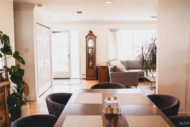 dining room featuring visible vents, a baseboard heating unit, crown molding, and light wood-style floors