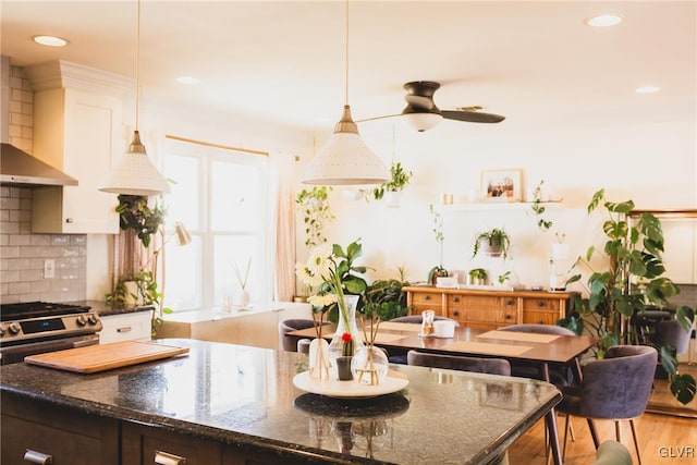 kitchen with tasteful backsplash, light wood finished floors, stainless steel range with gas stovetop, dark stone countertops, and wall chimney exhaust hood