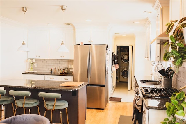 kitchen with a breakfast bar, backsplash, stacked washing maching and dryer, stainless steel appliances, and white cabinets