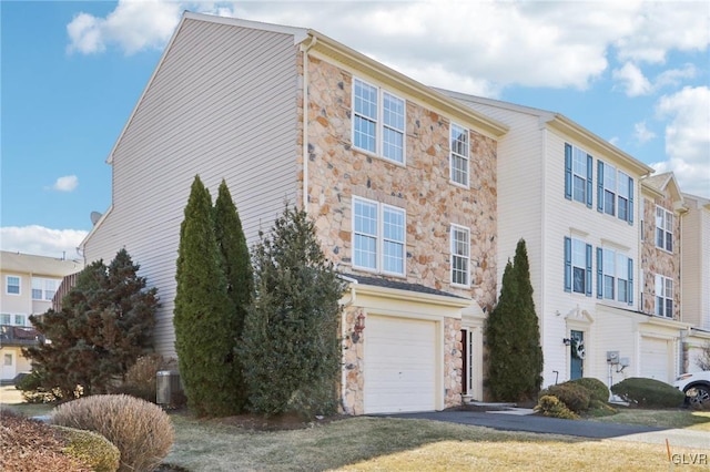 view of property featuring aphalt driveway, stone siding, and an attached garage