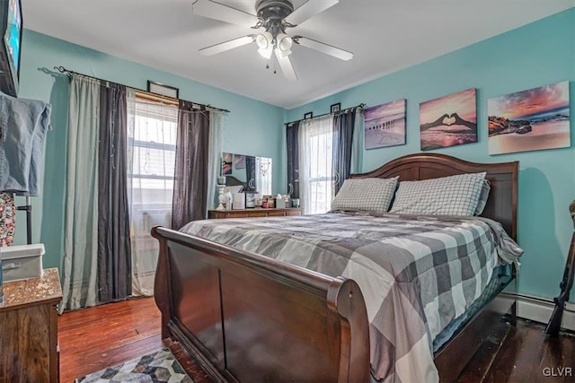 bedroom featuring a baseboard heating unit, multiple windows, a ceiling fan, and wood-type flooring