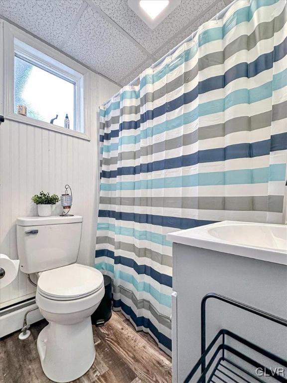 bathroom with a baseboard heating unit, a drop ceiling, toilet, wood finished floors, and vanity