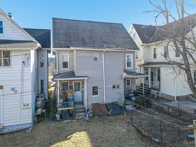 rear view of house with a shingled roof and fence