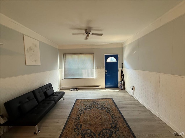 interior space with a ceiling fan, wood finished floors, a wainscoted wall, crown molding, and baseboard heating