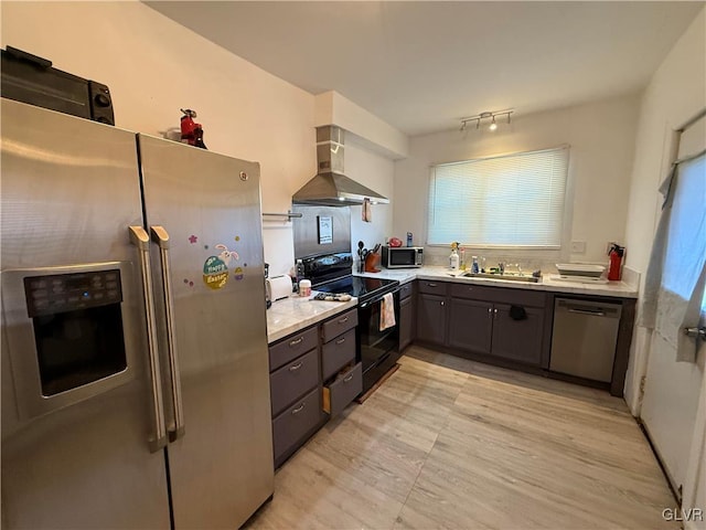 kitchen featuring light countertops, gray cabinets, appliances with stainless steel finishes, wall chimney exhaust hood, and a sink