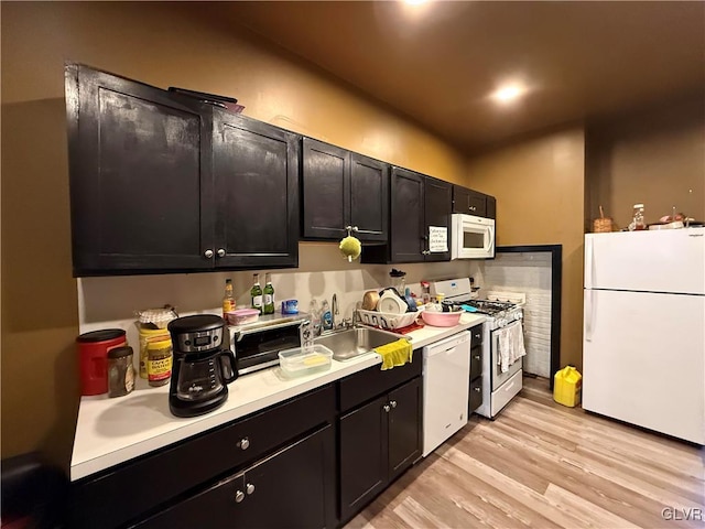 1131 Washington St, Easton, PA 18042 - kitchen featuring light countertops, dark cabinetry, light wood-style floors, white appliances, and a sink
