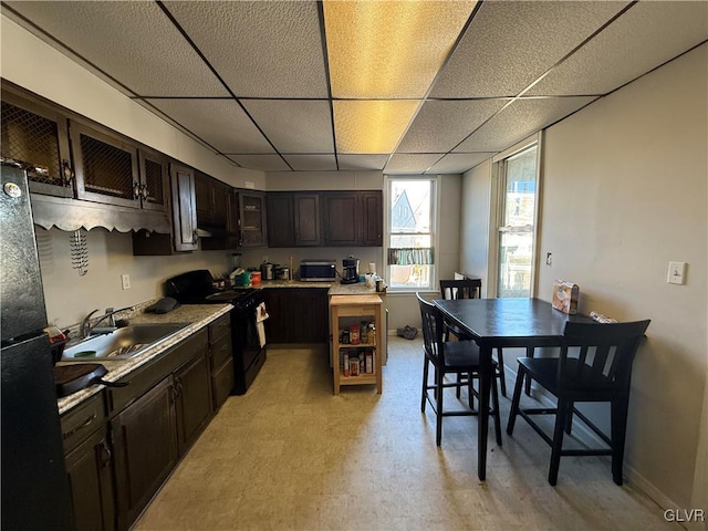 kitchen with black appliances, a sink, a drop ceiling, light countertops, and light floors