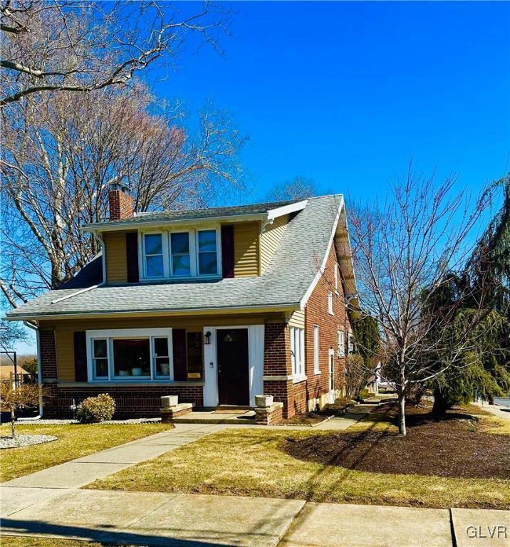 view of front of house featuring brick siding, a front lawn, a chimney, and roof with shingles