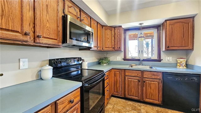 kitchen with decorative light fixtures, light countertops, brown cabinets, black appliances, and a sink