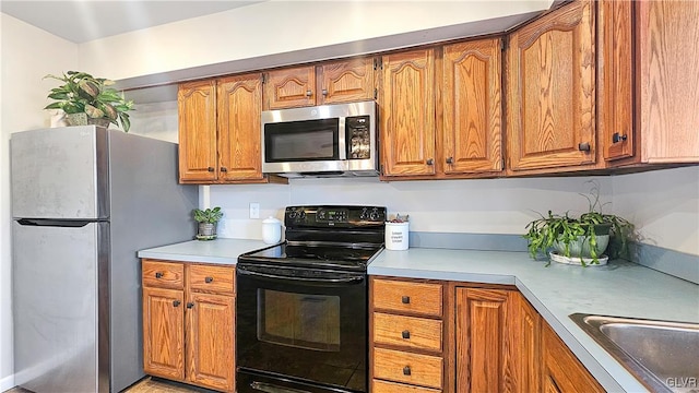 kitchen featuring brown cabinetry, stainless steel appliances, light countertops, and a sink