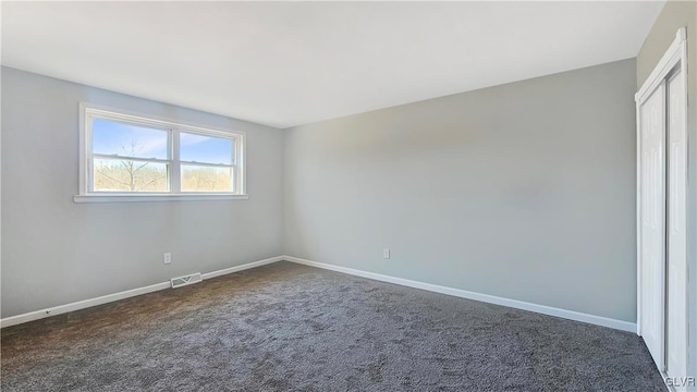 empty room with visible vents, dark carpet, and baseboards